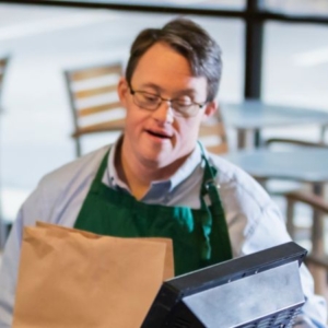 A man with Down syndrome and wearing an apron bags groceries at the grocery store
