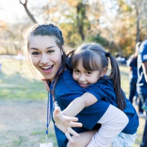 A smiling woman holds a smiling little girl on her back outside