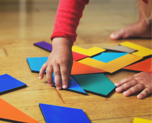 Close up view of child's hands playing with geometric shapes on wooden floor