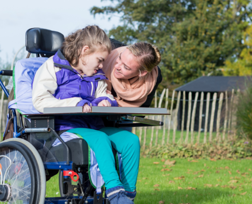 Young woman in a wheelchair with her caregiver smiling