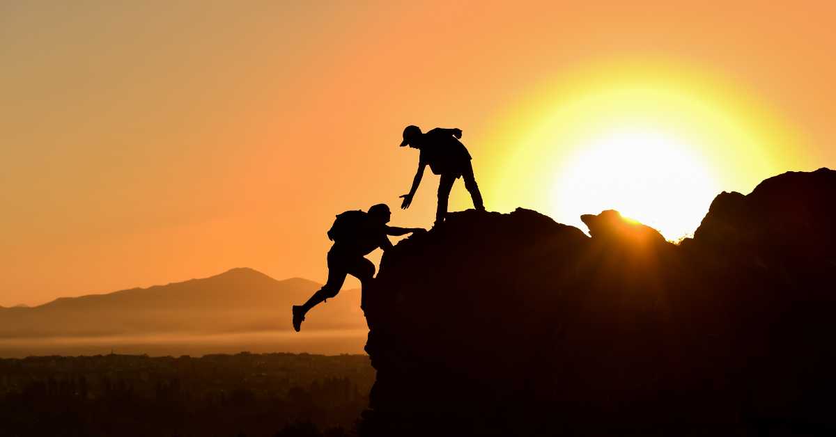 Human being helping another climb over a rock