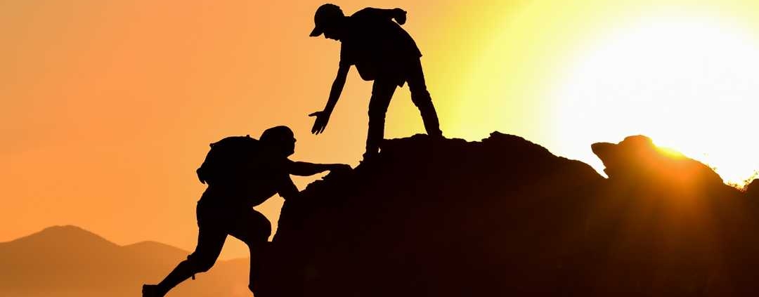 Human being helping another climb over a rock