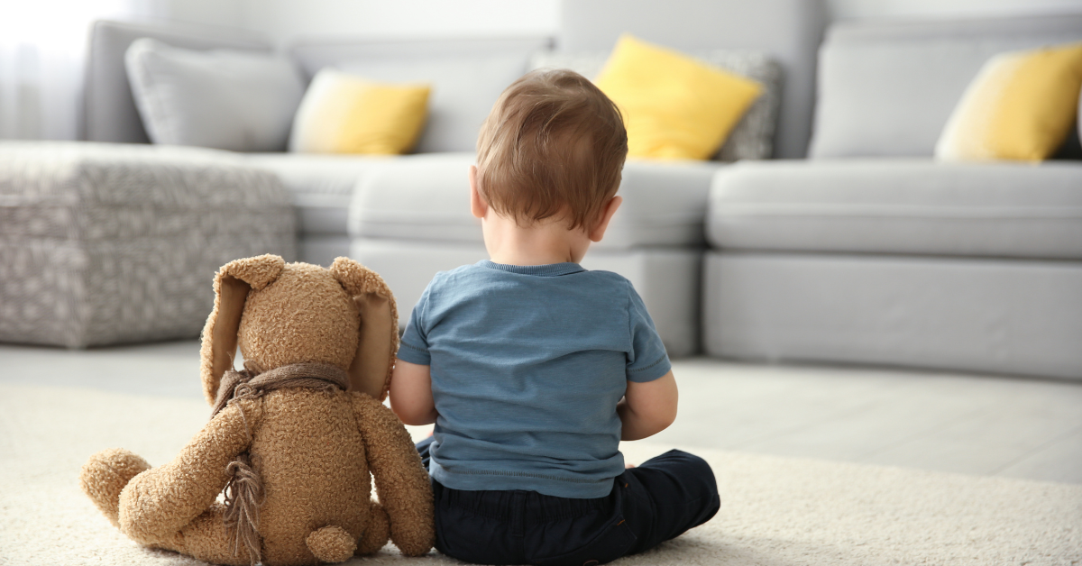 One year old baby with teddy bear sitting with back to camera