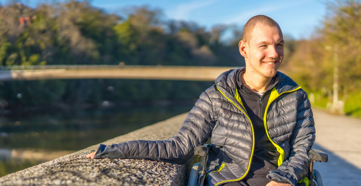man with developmental disability smiling outside while his hand is resting on a stone wall