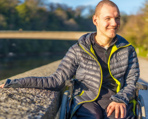 man with developmental disorder smiling outside while his hand is resting on a stone wall.