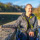 man with developmental disorder smiling outside while his hand is resting on a stone wall.