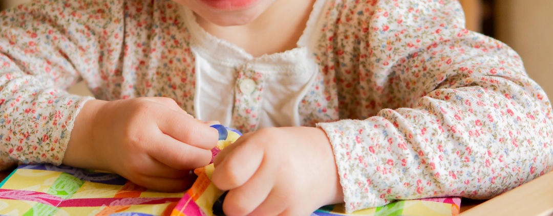 preschool aged girl with Down Syndrome smiling and working on a skills buttoning book at home