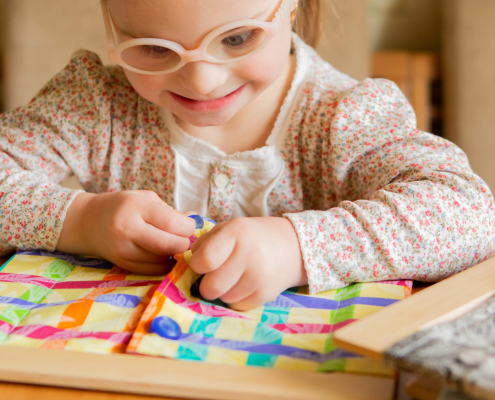 preschool aged girl with Down Syndrome smiling and working on a skills buttoning book at home